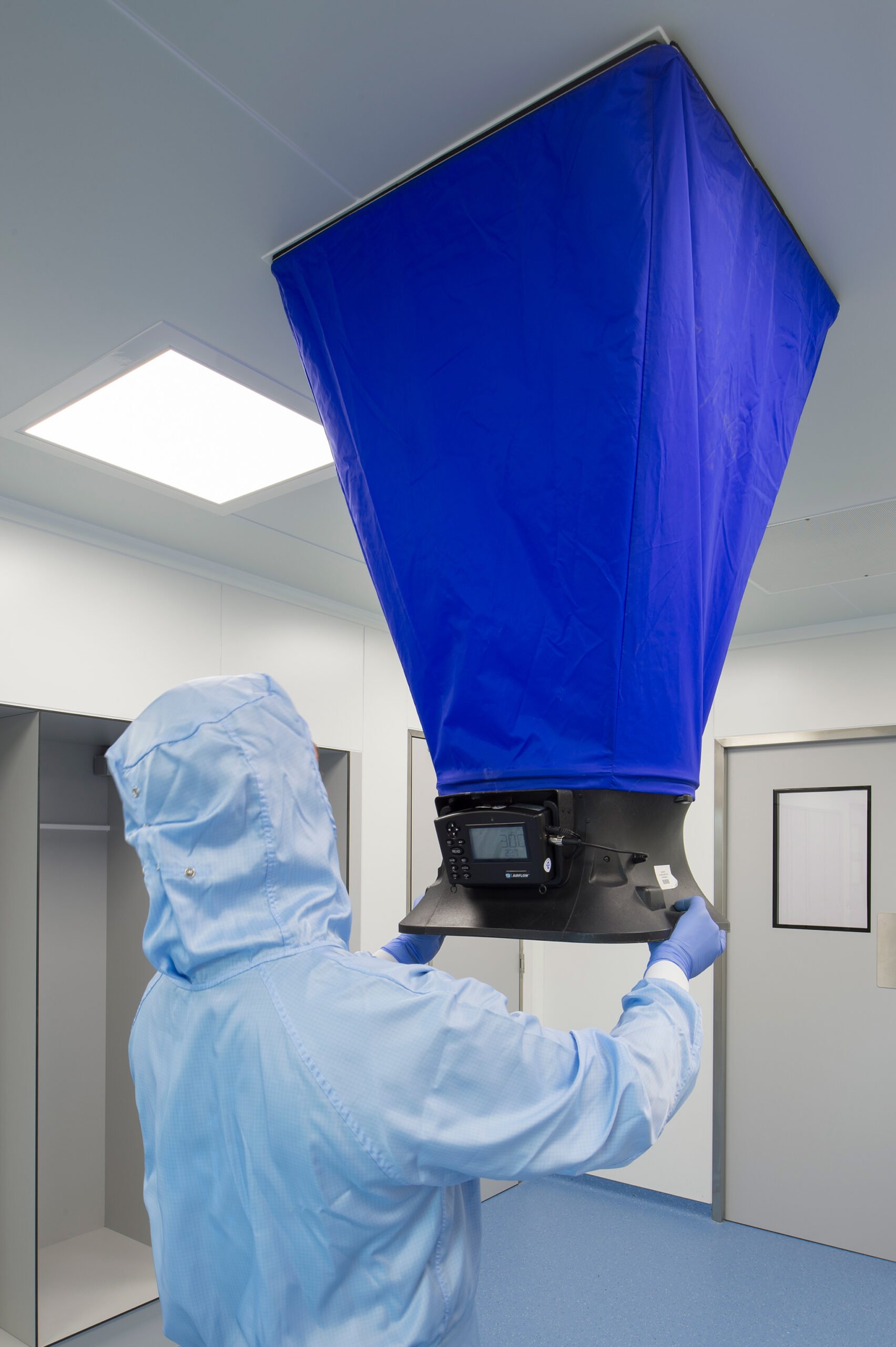 Technician performing airflow qualification in a cleanroom environment using specialized equipment.